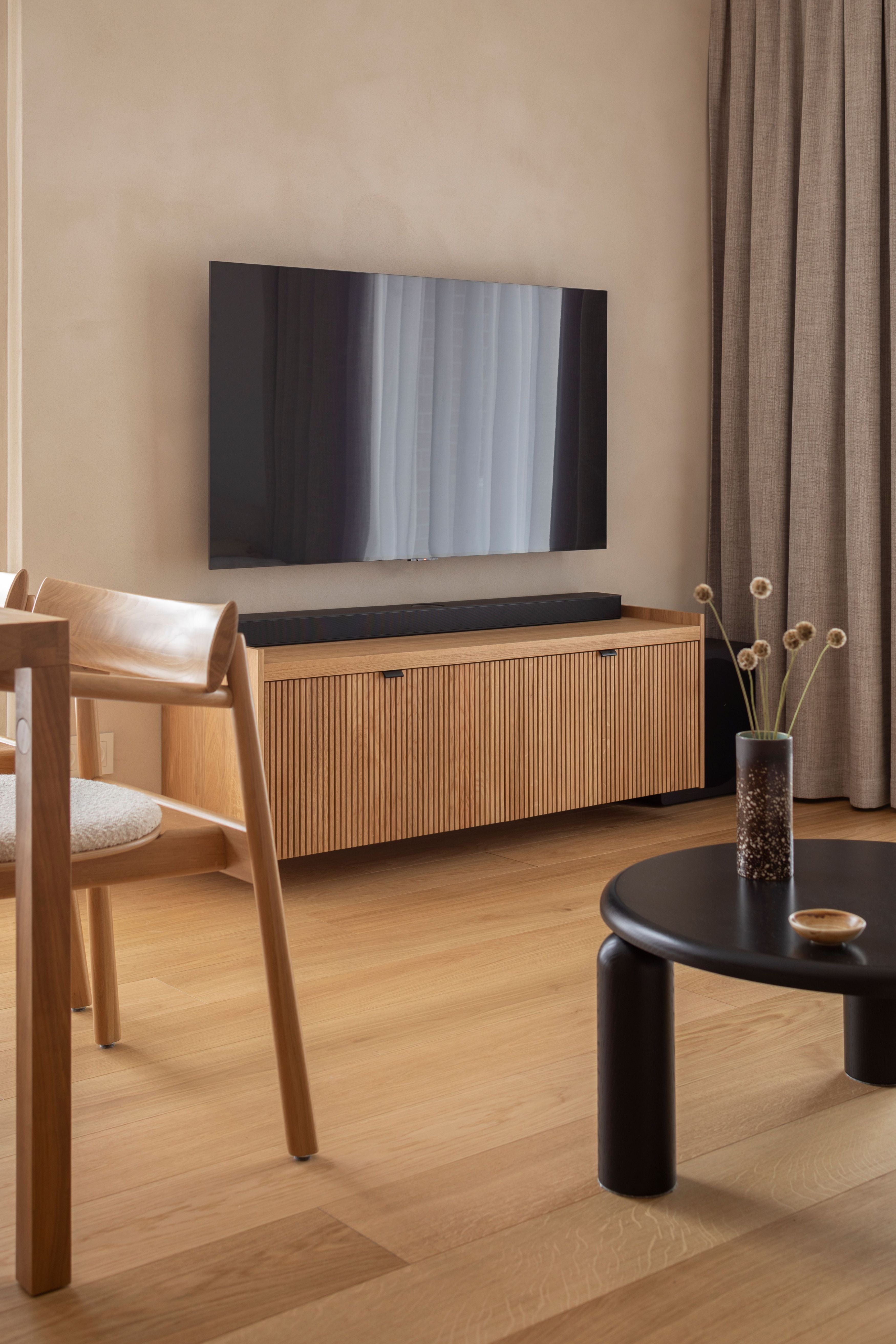 A wall-mounted wooden console with vertical slats, paired with a round wall mirror and a wooden shelf above.