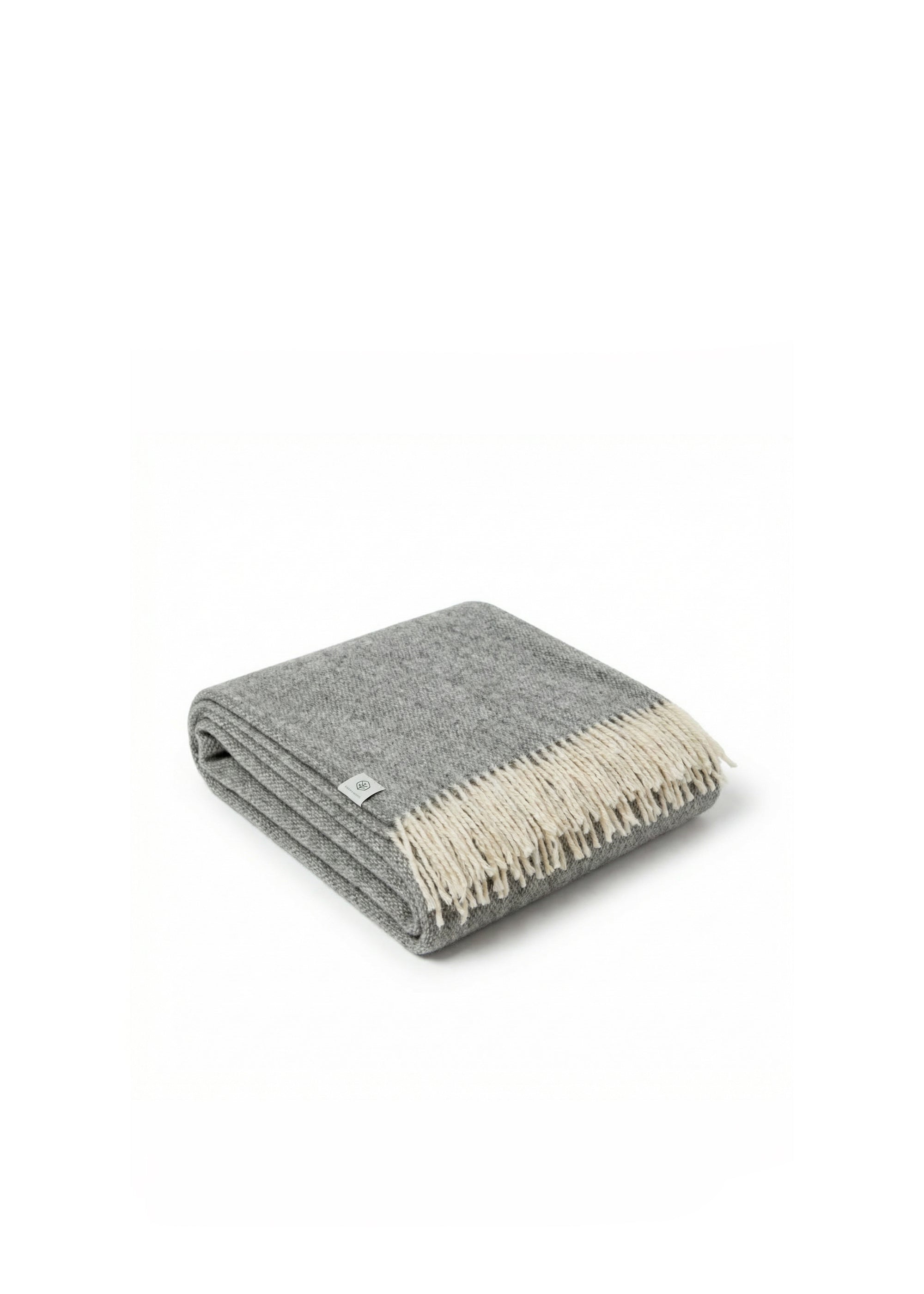 Rolled grey and cream wool throw blanket with fringed edges resting on a textured beige sofa