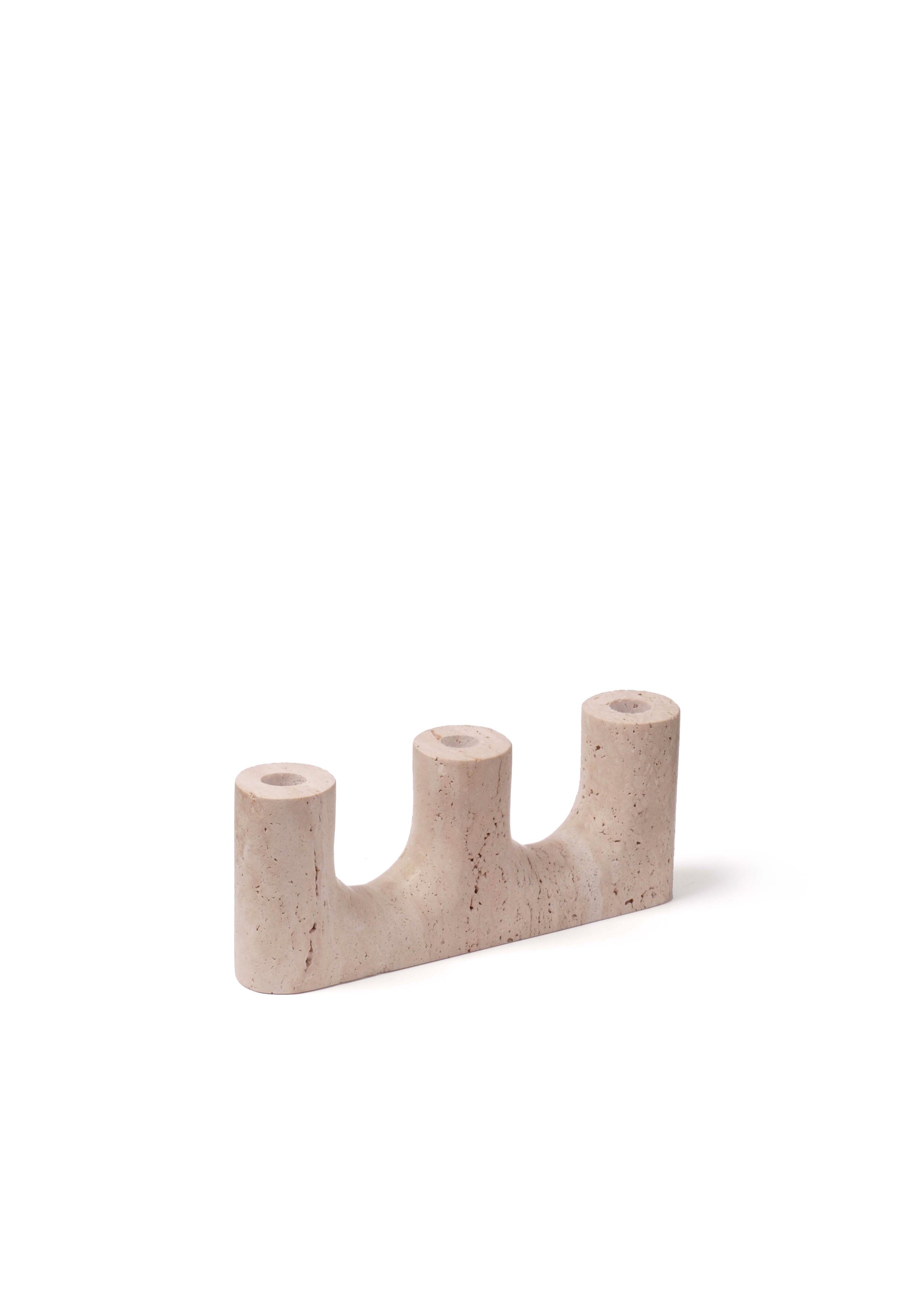 Three-slot beige stone candleholder with extinguished taper candles placed on a dark wooden cabinet