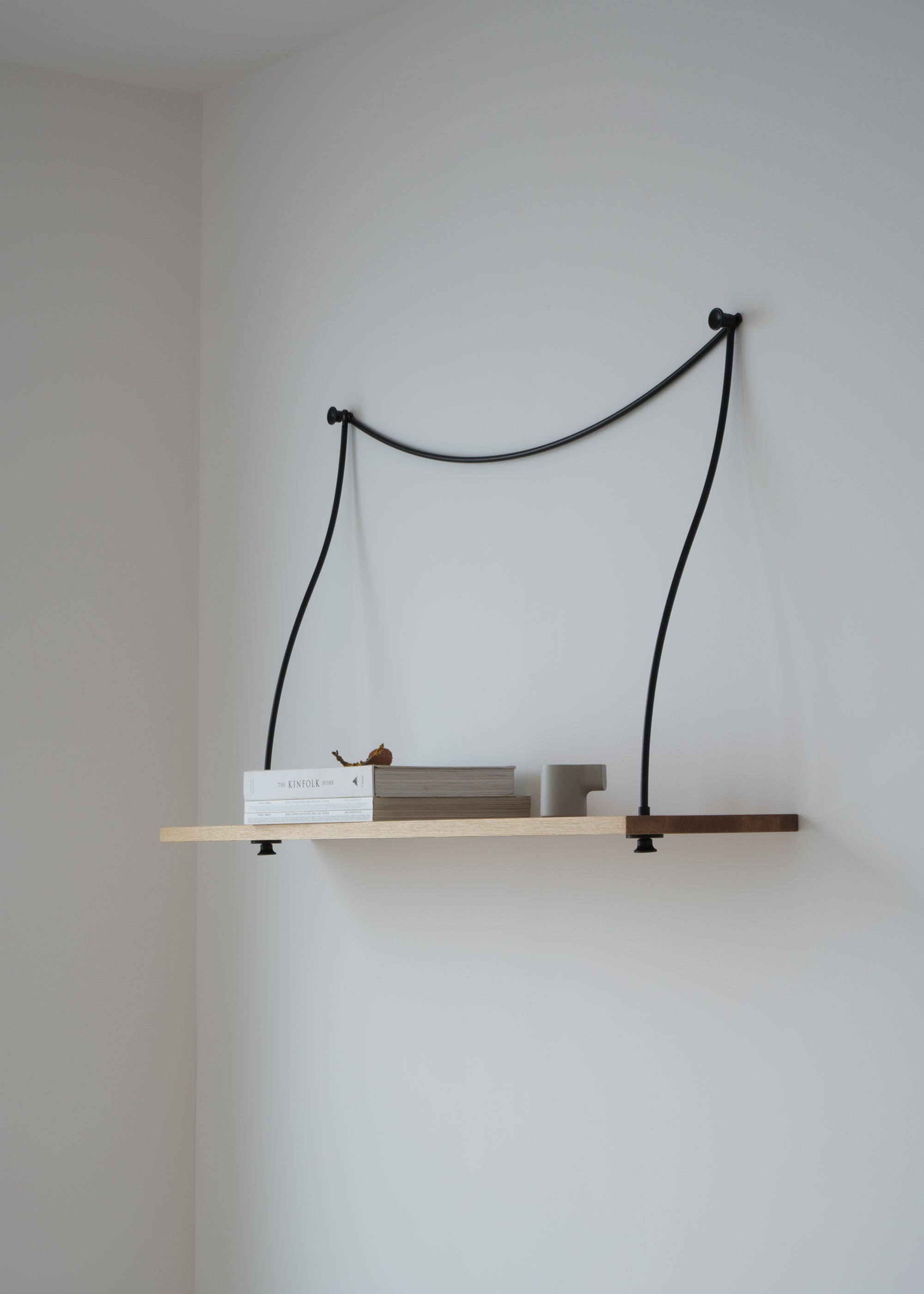 A wall-mounted wooden shelf supported by two curved black metal brackets, styled with books and small decor.