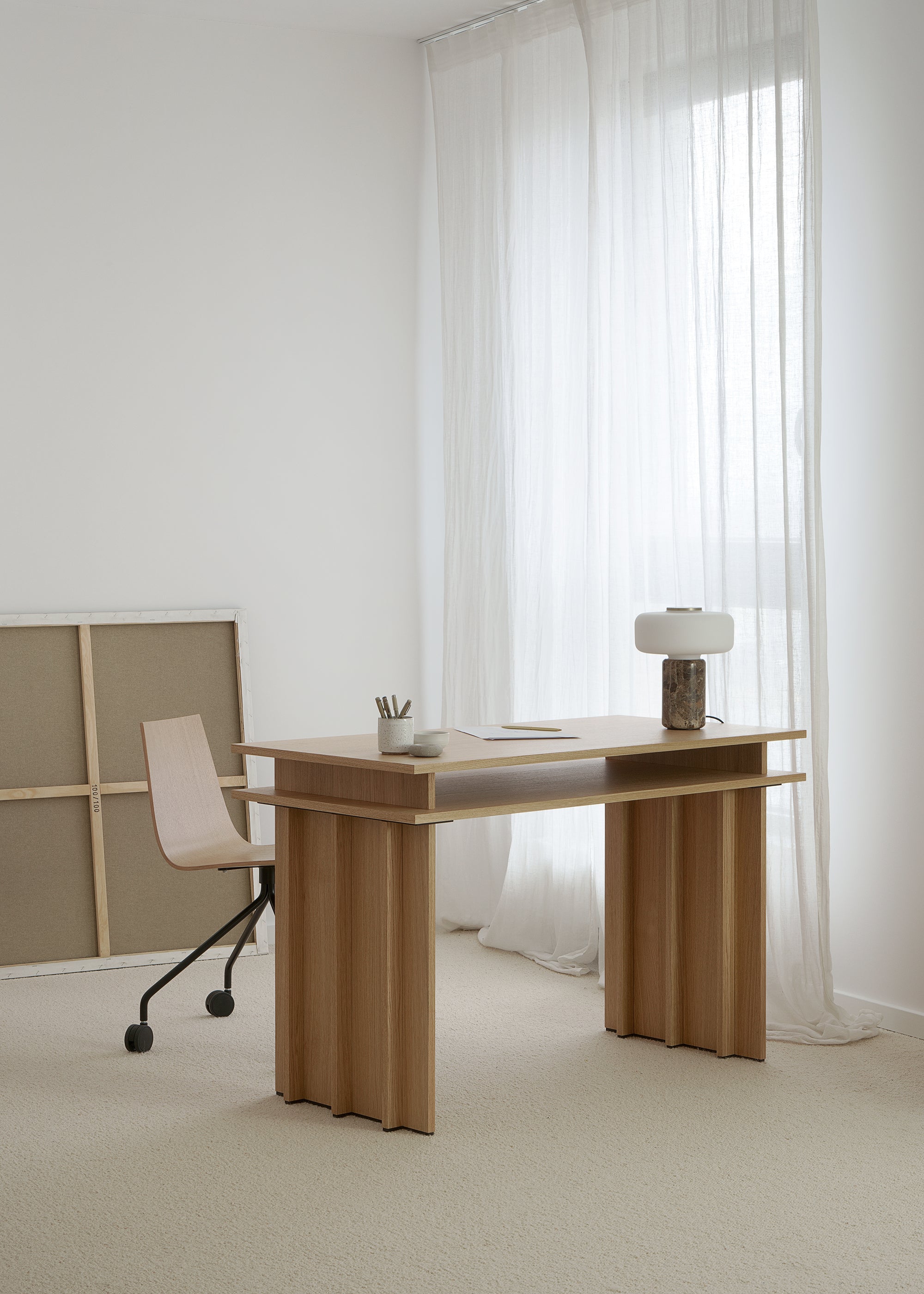 A light oak desk with a layered top and panel legs arranged in a bright workspace.